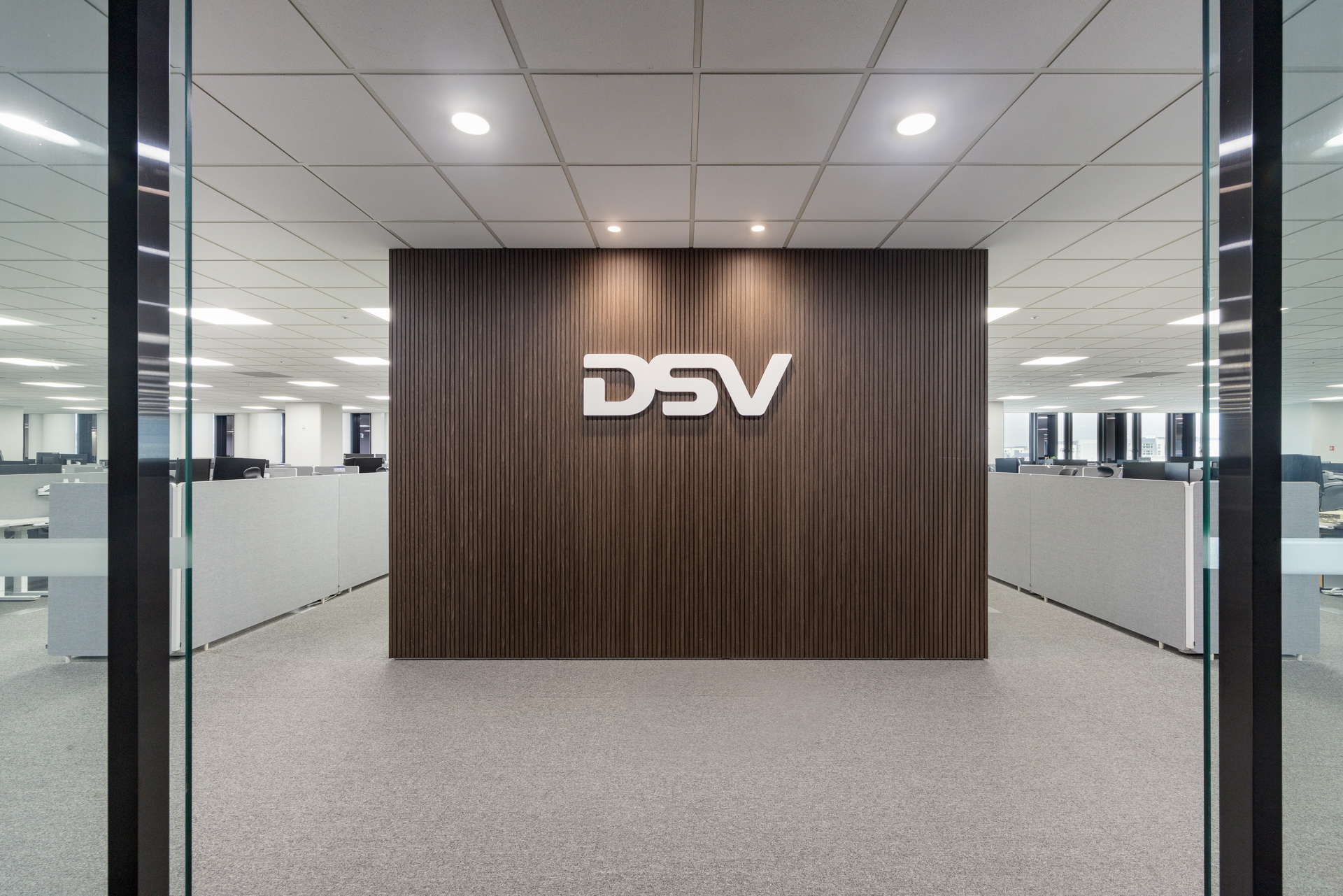 DSV 디에스브이에어앤씨 DSV Air & Sea 오피스 인테리어 - 시드나인 SIDnine 시공, 우드 루버 로고월과 유리 파티션 너머 오픈 오피스가 보이는 업무공간