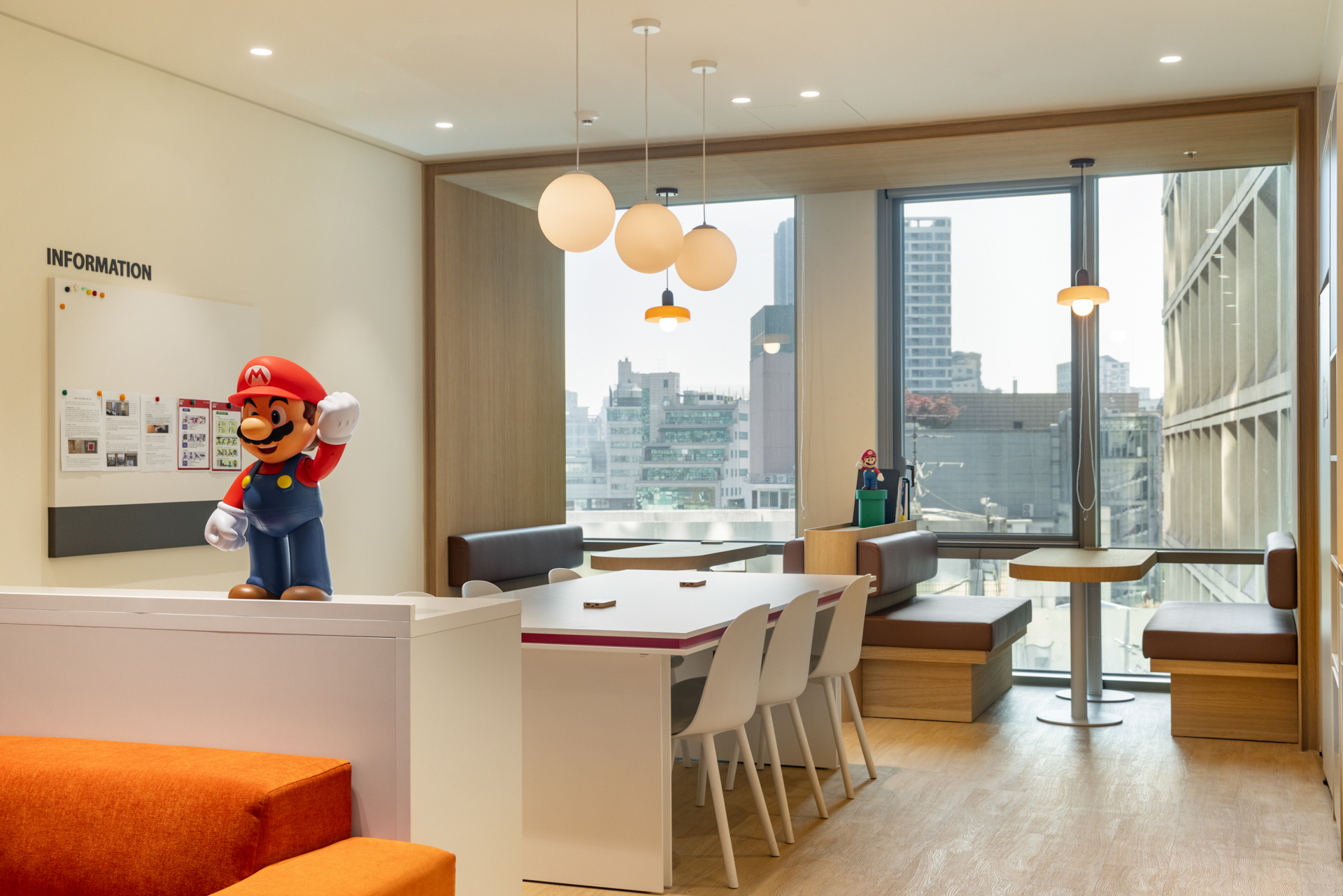 한국닌텐도(Nintendo Korea) 오피스 라운지의 인포메이션 보드와 마리오 피규어, 창가 벤치 좌석이 있는 휴게 공간, 시드나인(SIDnine) 시공 office lounge design