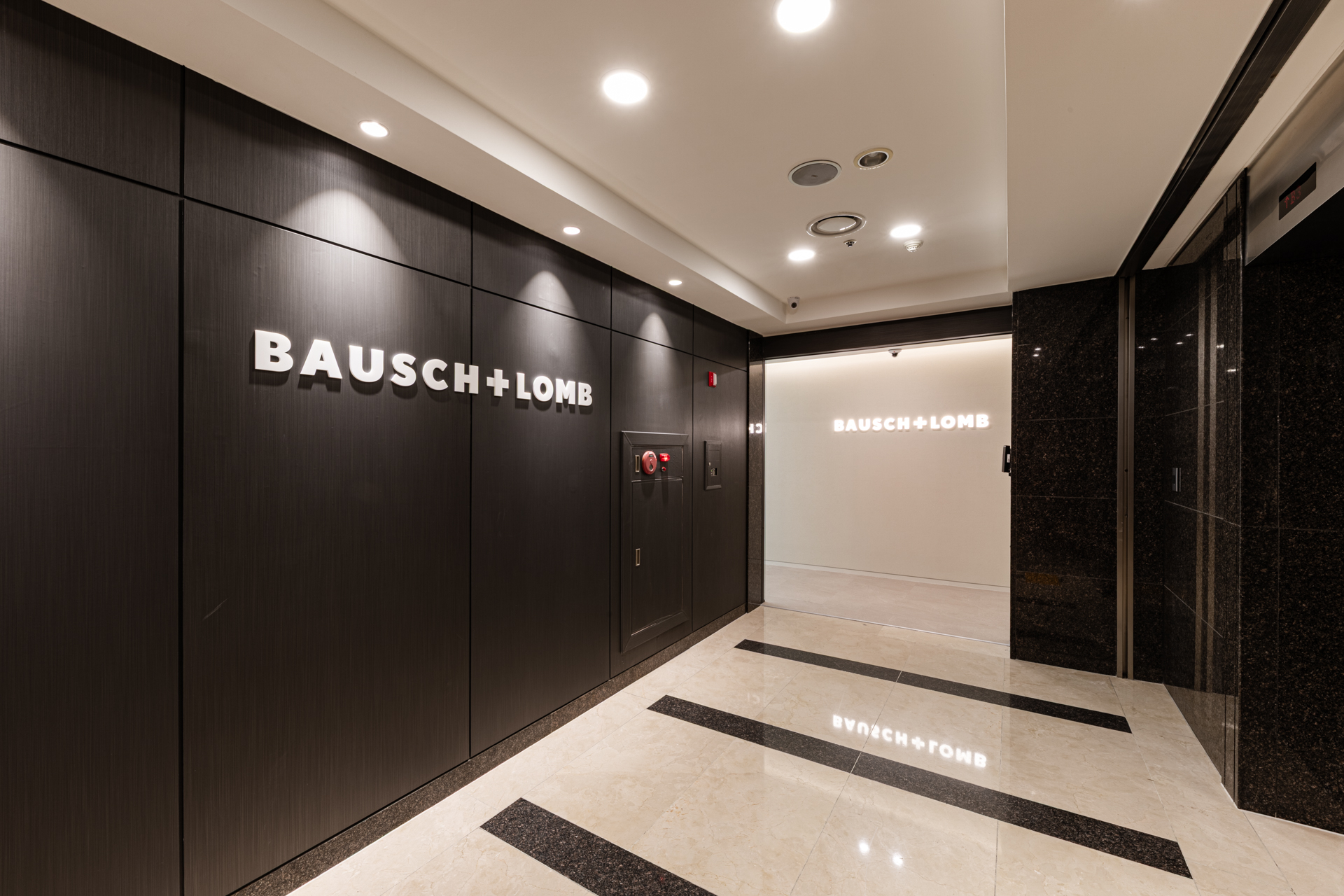 시드나인(SIDnine)이 시공한 바슈롬(Bausch + Lomb) 오피스 로비 공간, 블랙 월 마감과 Bausch + Lomb 로고가 강조된 기업 인테리어