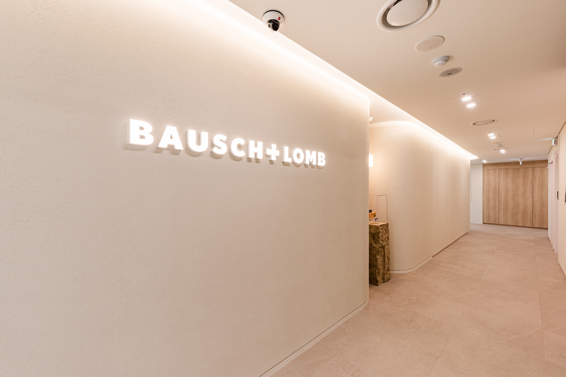 시드나인(SIDnine) 시공 바슈롬(Bausch + Lomb) 사무실 복도 전경, 곡선형 벽체와 간접조명이 적용된 모던 오피스 인테리어